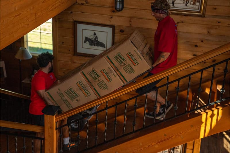 Movers carry moving boxes up a wooden staircase inside a log home