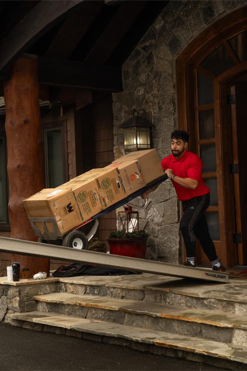 A mover wheels a hand truck stacked with boxes down a ramp from a stone entryway