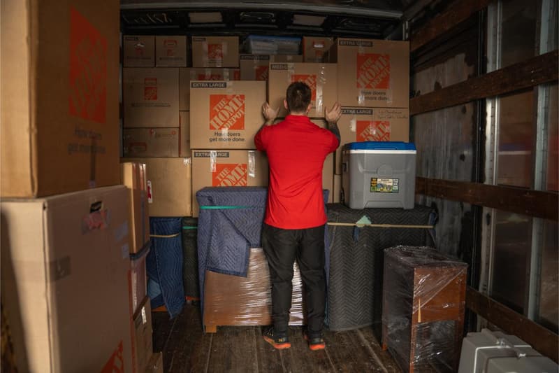 A mover in a red shirt stacks packed boxes and padded furniture tightly inside a moving truck