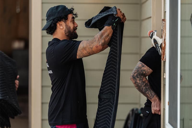 Movers in black 7B Moving shirts drape padded moving blankets over a doorway