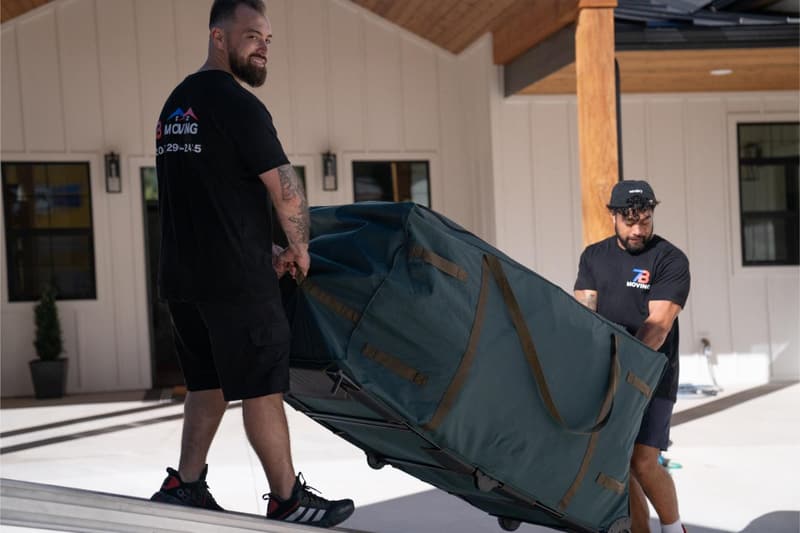 Two movers carry a large blanket-wrapped item out of a bright modern house