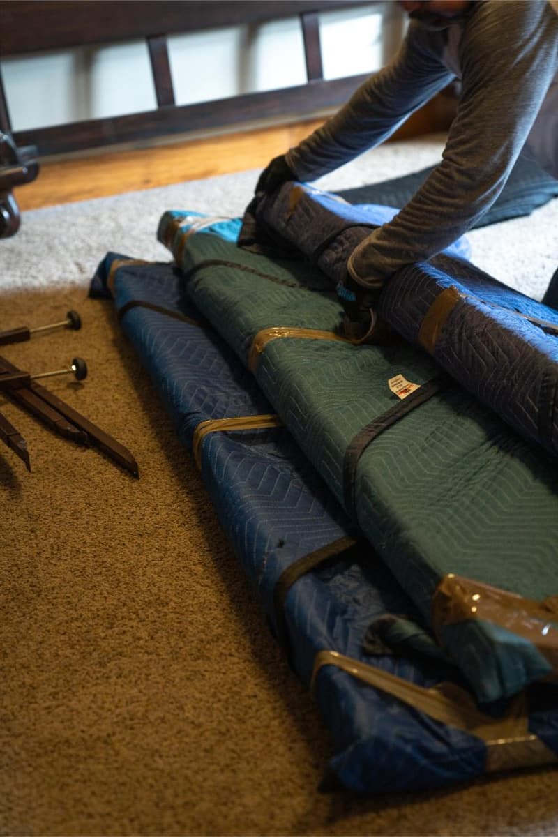 Furniture pieces wrapped in green and blue moving pads laid out on a carpeted floor
