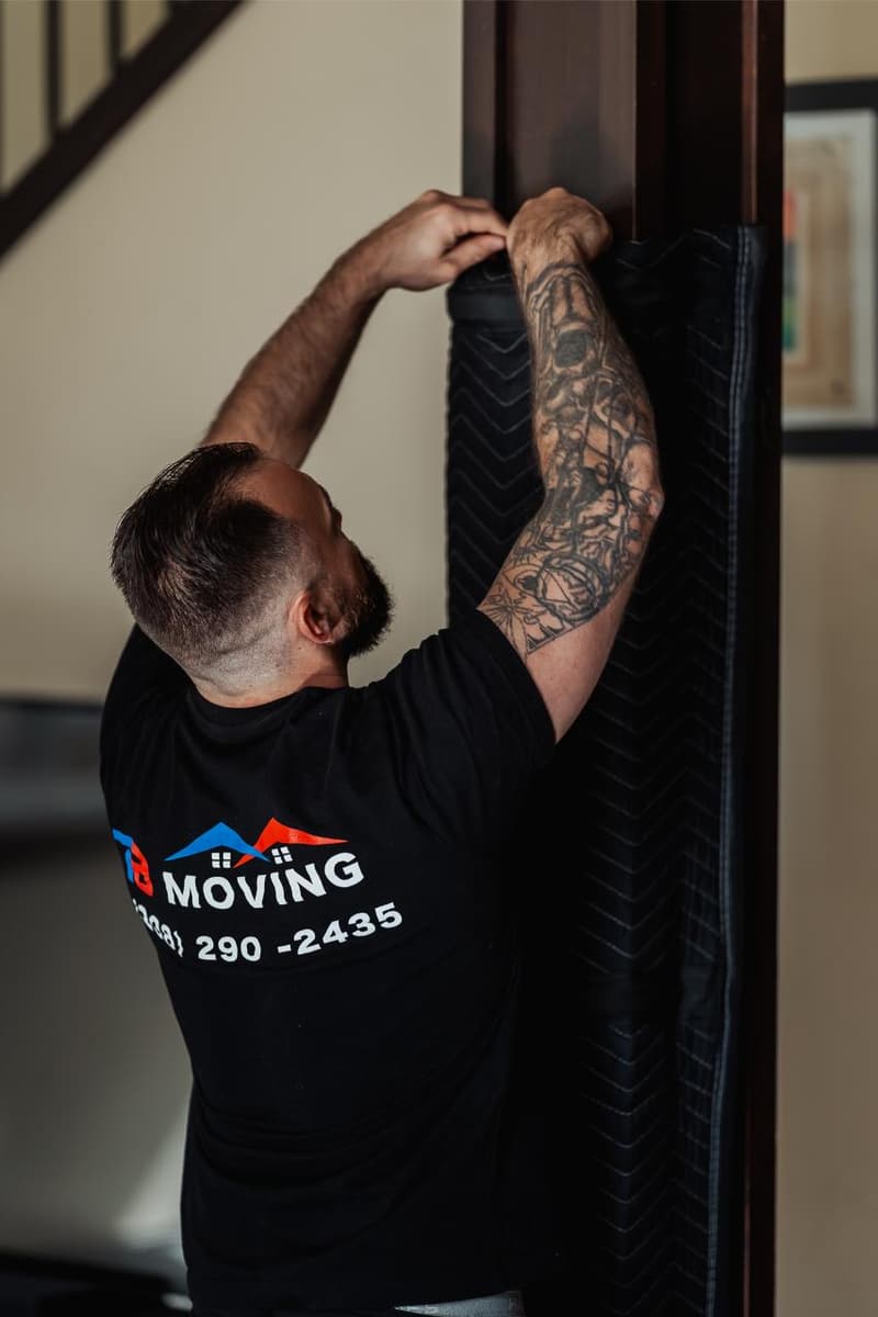 A mover in a 7B Moving shirt hangs a protective blanket over a door frame