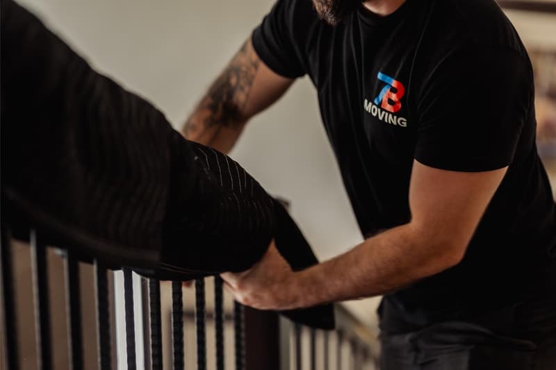 A 7B Moving crew member wraps a wooden stair railing with a moving blanket to protect it