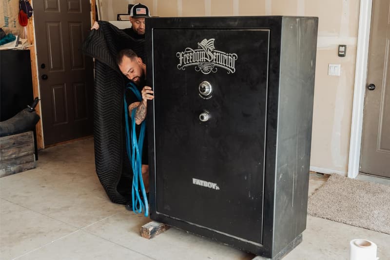 A mover tilts a large black gun safe onto a blue stair-climbing dolly inside a garage