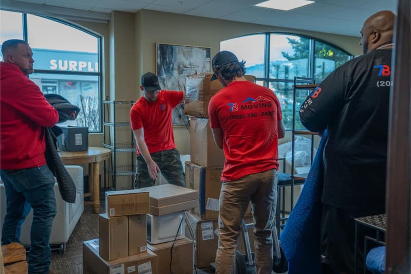 Several movers stage packed boxes and wrapped items in a bright room
